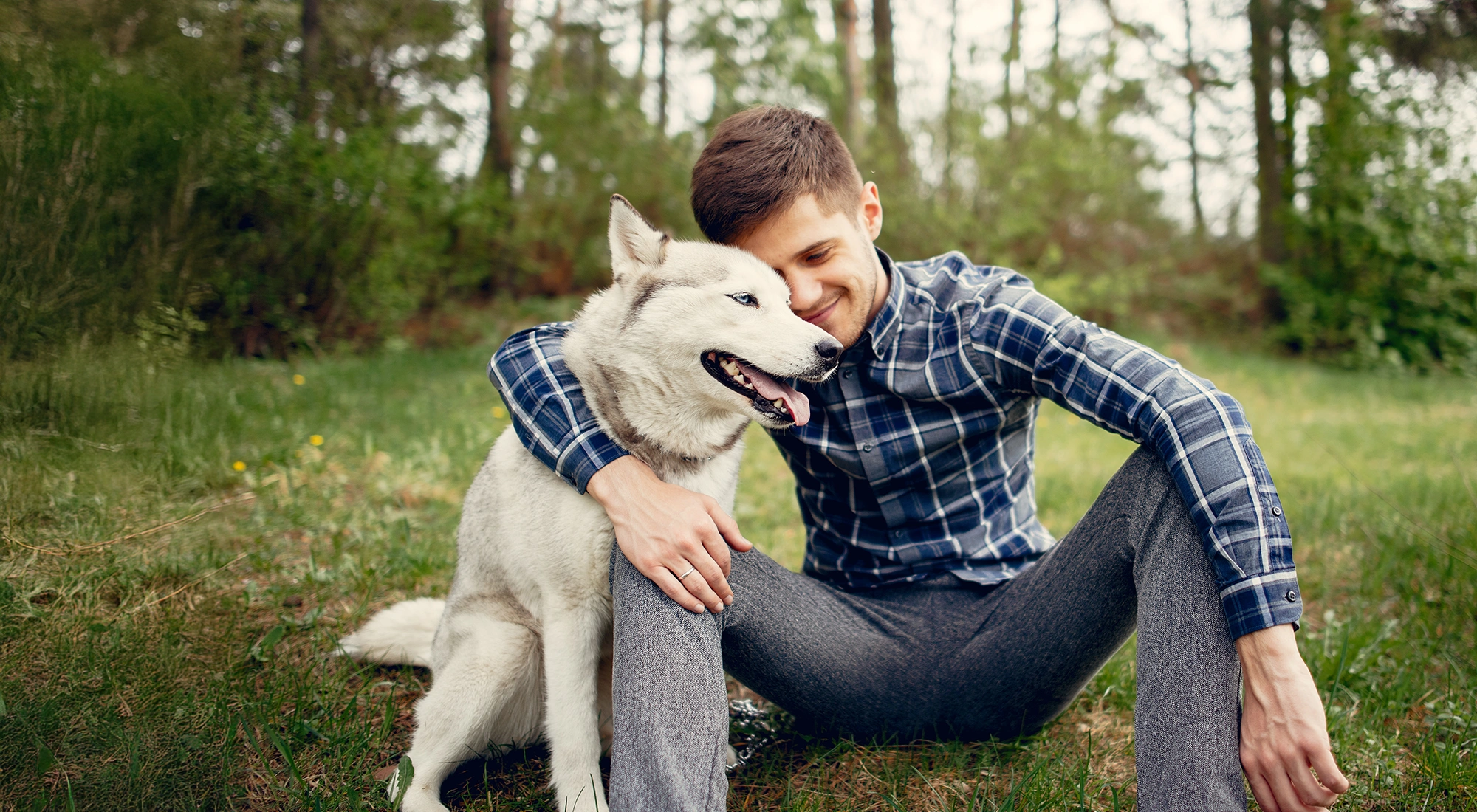 young man hugging his white dog while sitting on the ground outside